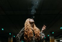 Hübsche rothaarige Frau raucht auf verschwommenem Parkplatz — Stockfoto