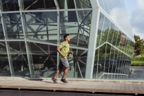 Homem étnico jogging contra edifício moderno na cidade — Fotografia de Stock