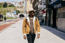 Nero uomo in cappello e occhiali da sole a piedi sulla strada — Foto stock