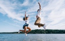 Woman and man in casual clothes having fun on lake and laughing with blue sky and forest on background — Stock Photo
