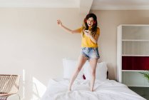 Girl dancing on bed with smartphone — Stock Photo