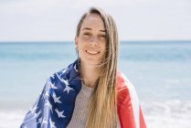 Портрет молодой женщины, позирующей на пляже с флагом США . — стоковое фото