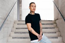 Молодой красивый мужчина с татуировками на шее и руках, стоящий на лестнице и смотрящий в камеру — стоковое фото