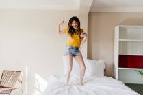 Girl dancing on bed with smartphone — Stock Photo