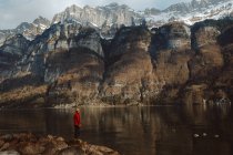 Vue latérale d'un touriste adulte debout au bord d'un lac calme dans les montagnes, Walensee, Suisse — Photo de stock