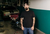 Mecânico tatuado em pé na garagem — Fotografia de Stock