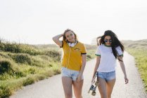 Teenage girls with longboard walking on road — Stock Photo