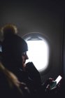 Mujer bonita mira el teléfono móvil sentado en la ventana del avión . - foto de stock