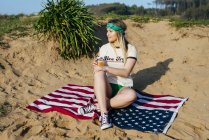 Девушка с выпивкой сидит на американском флаге — стоковое фото