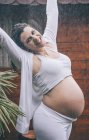 Excited pregnant woman standing in rain against wooden house — Stock Photo