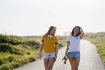 Девушки-подростки с длинной доской прогулки по дороге — стоковое фото