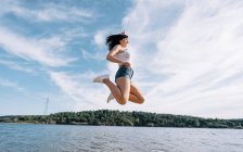 Mulher alegre salta junto ao lago. — Fotografia de Stock