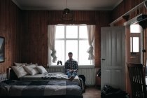 Взрослый мужчина сидит и отдыхает на кровати во время использования смартфона дома в Исландии — стоковое фото