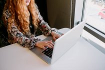 Cheerful pretty redhead woman sitting at laptop and typing at the table. — Stock Photo