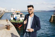 Uomo con zaino e smartphone in piedi in porto — Foto stock