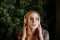 Jolie jeune rousse femme mettre des écouteurs à la brousse. — Photo de stock
