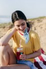 Дівчина-підліток з напоєм сидить на піску — стокове фото