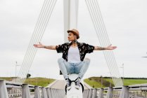 Hipster sitting on railing of bridge — Stock Photo