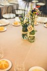 Belles fleurs rustiques lumineuses en bouteille sur la table à banquette servie. — Photo de stock