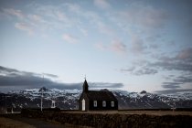 Маленька чорна будівля церкви розміщена на полі біля сніжних гір в Ісландії. — стокове фото