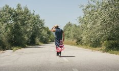 Человек с американским флагом идет по дороге — стоковое фото