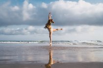 Girl doing exercises on beach with cloudy sky on background — Stock Photo