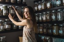 Femme souriante prenant pot avec épice dans le magasin en regardant la caméra — Photo de stock