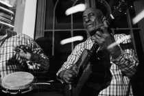 Зрелые кубинские музыканты, выступающие в ночном клубе, черно-белый кадр с длительной экспозицией — стоковое фото