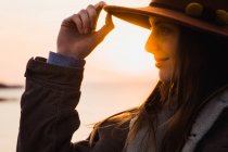 Verträumte Frau mit Hut am Meer bei Sonnenuntergang — Stockfoto