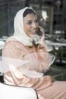 Moroccan woman with hijab and traditional Arabic dress talking on phone behind window pane — Stock Photo