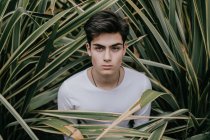 Bello giovane adolescente alla moda in piedi in un cespuglio verde — Foto stock