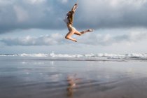 Chica saltando en la playa con cielo nublado en el fondo - foto de stock