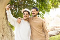 Smiling happy male friends taking selfie with smartphone in sunny park — Stock Photo