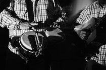Обрезанные мужчины-музыканты, играющие на барабанах и гитаре в ночном клубе, черно-белый кадр с длительной экспозицией — стоковое фото