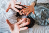 Joven hombre y mujer acostados en la cama y posando con las manos arriba en casa - foto de stock