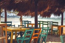 Cadeiras coloridas vazias e mesas de café ao ar livre sob abrigo na costa do mar do Caribe, México — Fotografia de Stock