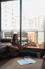 Mujer tocando la guitarra mientras está sentado en el suelo en casa - foto de stock