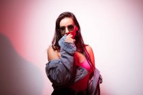 Pretty young pink dressed woman in sunglasses standing at white wall and looking at camera — Stock Photo
