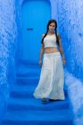 Woman wearing white top and long skirt walking on Moroccan city dyed blue — Stock Photo