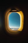 Shot from inside of airplane window with blue sky behind illuminated with golden lights of sunset — Stock Photo