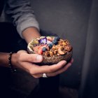 Manos de persona irreconocible sosteniendo un tazón lleno de sabrosas frutas y frutos secos. - foto de stock