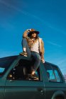 Stylish woman in hat sitting on car roof — Stock Photo