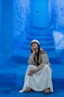 Mujer pensativa sentada en las escaleras en la ciudad marroquí teñido de azul - foto de stock