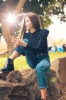 Junge Frau sitzt auf Felsen und hält Smartphone im Park — Stockfoto