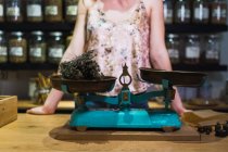 Woman standing near vintage scales with thyme in shop — Stock Photo