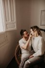 Homem sentado em poltrona e tocando nariz da namorada em casa — Fotografia de Stock