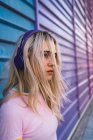 Молода блондинка з фіолетовими навушниками стоїть перед барвистою стіною — стокове фото