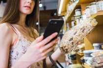 Donna che naviga smartphone mentre sceglie il cibo in negozio — Foto stock