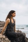Nachdenklich lächelnde Frau sitzt auf einem Felsen am Meer — Stockfoto