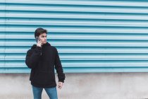 Jovem adolescente em pé na parede de metal e falando no smartphone na rua — Fotografia de Stock